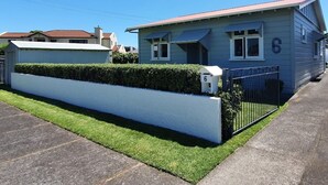 Una casa de un piso con fachada azul claro, un muro frontal blanco y una cerca de metal negro.