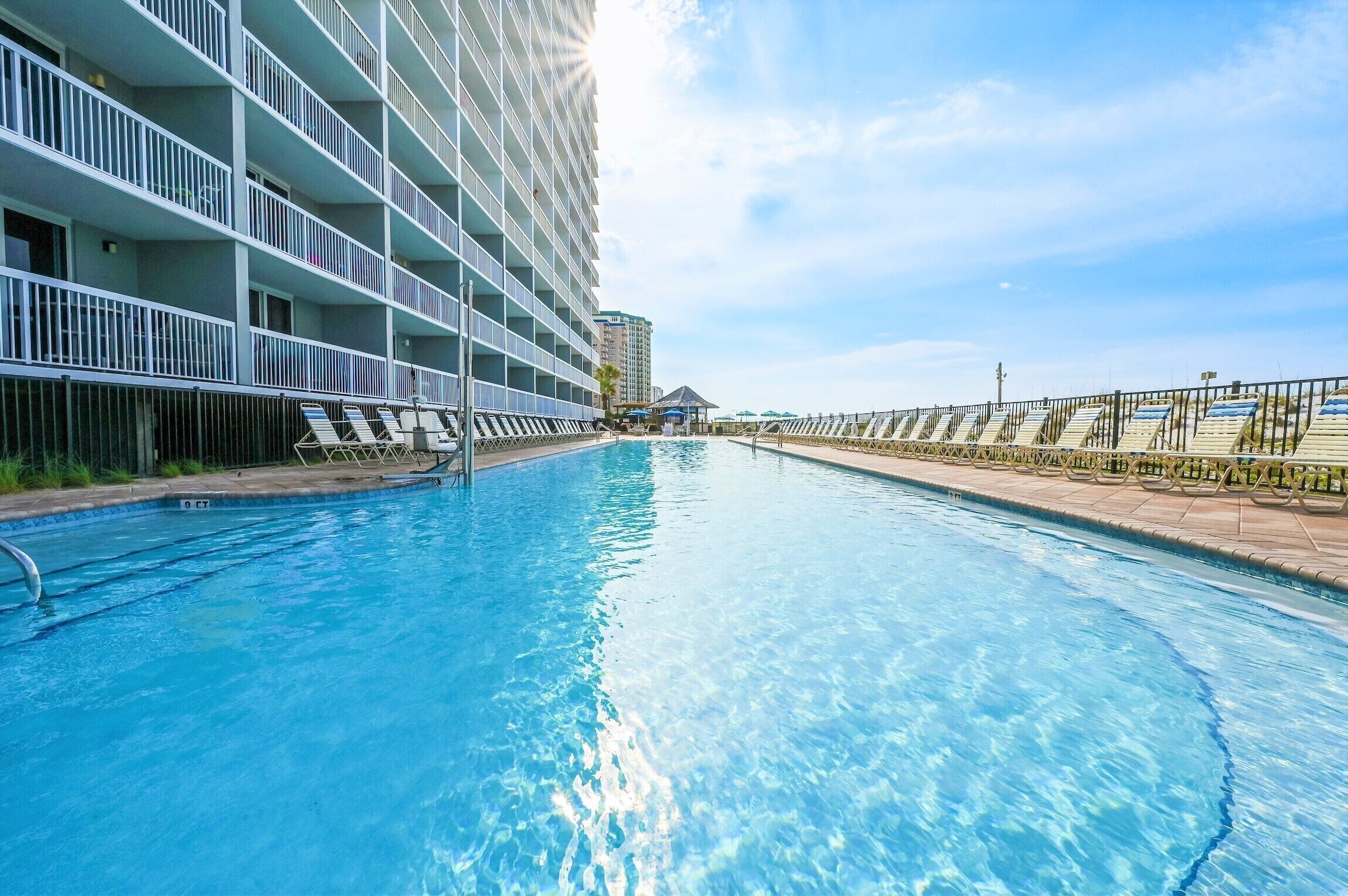A swimming pool with sunbathing loungers and a high-rise building in the background.