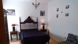 A bedroom with a wooden bed, two bedside tables with lamps, a chair, and wall art. - Jardim da Maresia was renovated for your convenience and unforgettable holidays. (São João das Lampas)