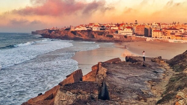 A coastal town with a rocky shoreline, buildings along the coast, and a person standing on the rocks. - Jardim da Maresia was renovated for your convenience and unforgettable holidays. (São João das Lampas)
