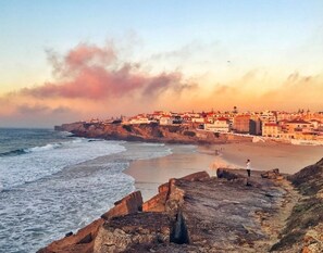 Un pueblo costero con un litoral rocoso, edificios a lo largo de la costa y una persona de pie sobre las rocas.