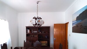 A dining area with a wooden table and chairs, a chandelier, a bookshelf, and a door leading to another room. - Jardim da Maresia was renovated for your convenience and unforgettable holidays. (São João das Lampas)
