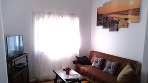 A living room with a television, a sofa, a coffee table, and a painting on the wall. - Jardim da Maresia was renovated for your convenience and unforgettable holidays. (São João das Lampas)
