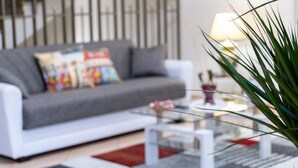 Una sala de estar moderna con un sofá gris, almohadones coloridos, una mesa de centro de vidrio y una planta.