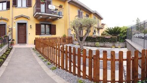 Un edificio amarillo con cerca de madera, un camino pavimentado y un árbol pequeño.
