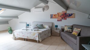 Un dormitorio con una cama, un sofá, una planta en maceta y obras de arte en la pared.
