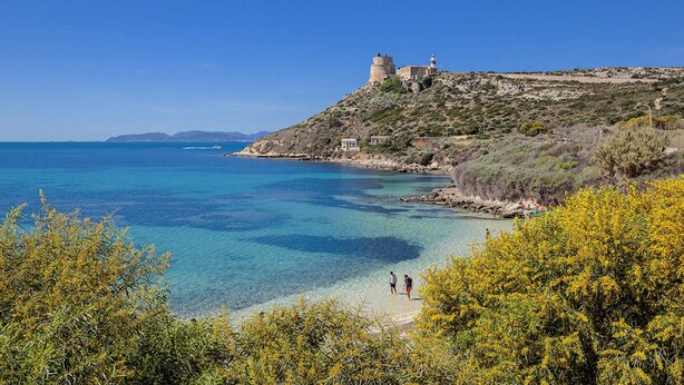 A coastal landscape with clear blue waters, a lighthouse, and a castle-like structure on a hill.