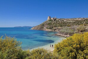 A coastal landscape with clear blue waters, a lighthouse, and a castle-like structure on a hill.