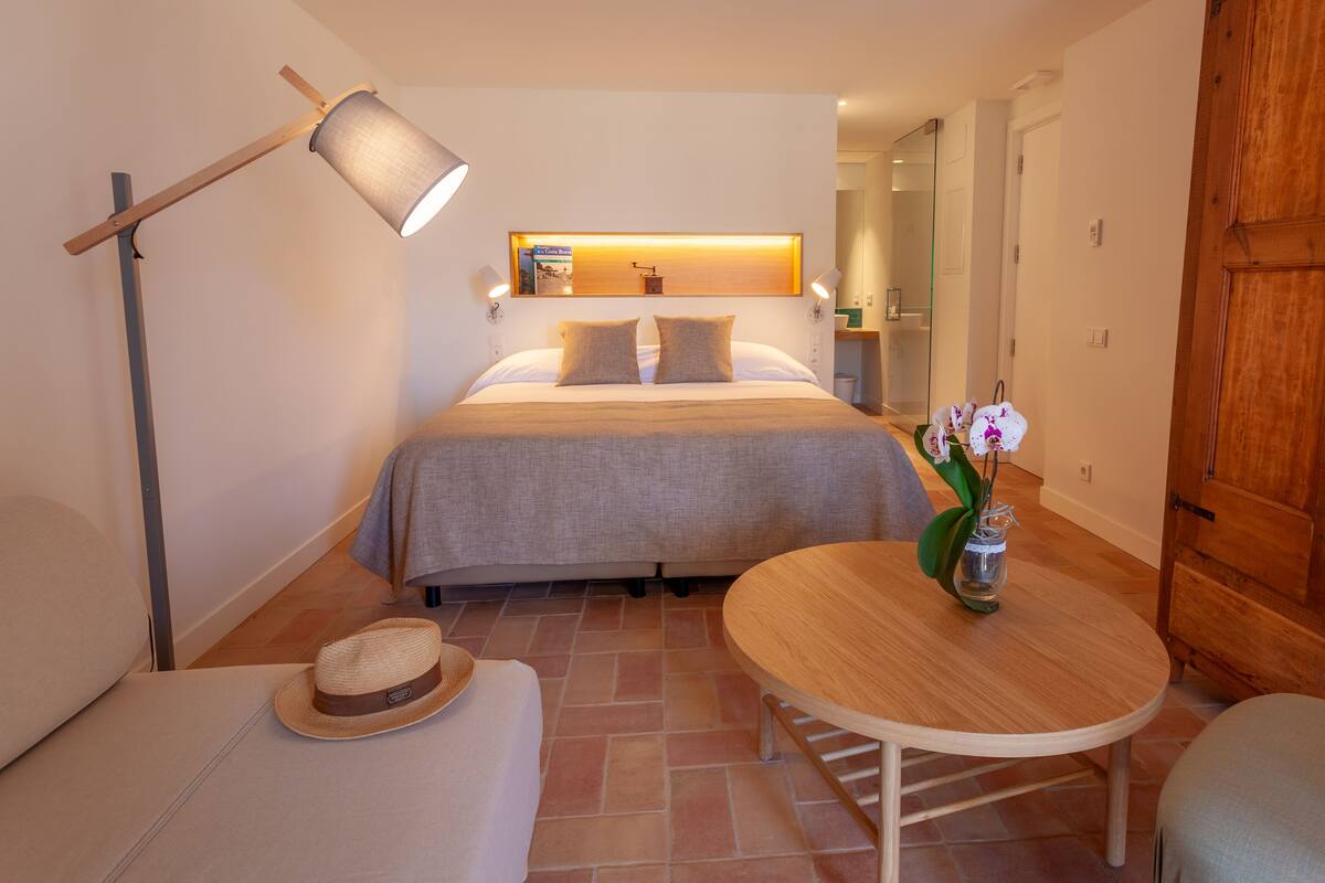A hotel room with a bed, a bedside table with a vase of flowers, a lamp, and a wooden wardrobe.