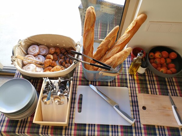 A table with a basket of bread, a bowl of tomatoes, and a cutting board with a knife. - Hotel Can Liret (Palafrugell)