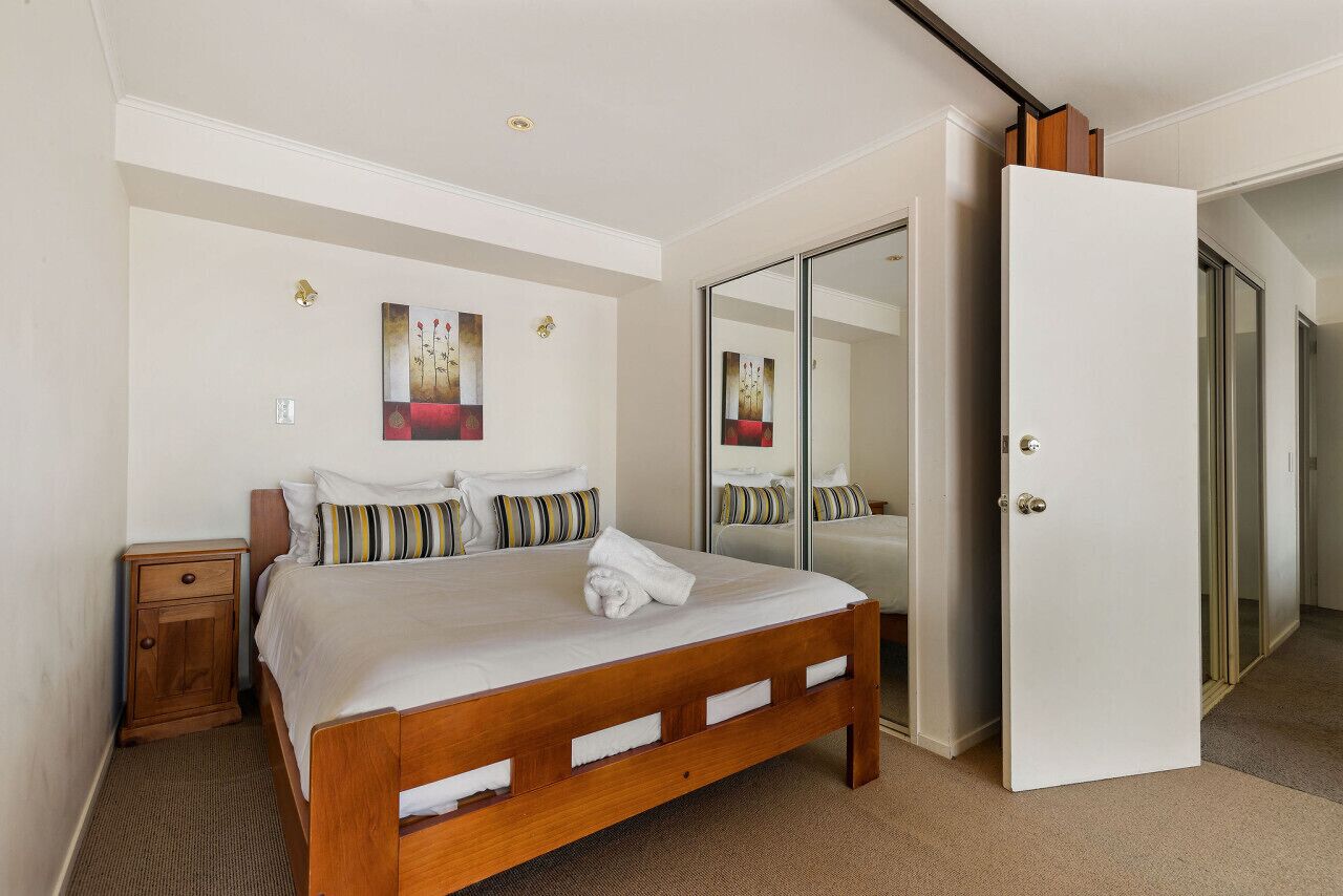 A bedroom with a wooden bed, a nightstand, a large mirror, and a sliding door leading to another room.