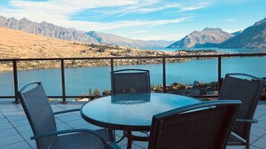 Une terrasse avec une table ronde et des chaises, donnant sur un lac et des montagnes.