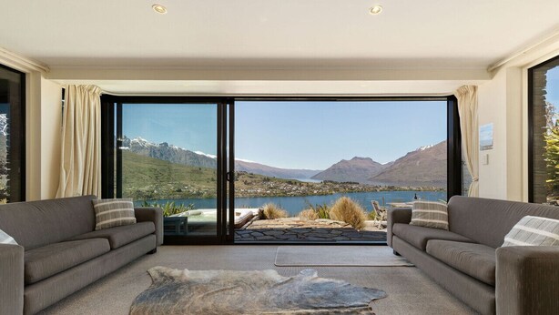 Un salon moderne doté d’une grande porte-fenêtre coulissante qui donne sur un paysage magnifique, avec un lac et des montagnes en toile de fond.