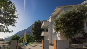 A modern building with a pool area, outdoor seating, and a mountain backdrop.