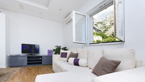 A modern living room with a white sofa, a television, and a window with a mountain view.