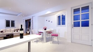 A modern living room with a white sofa, a dining table with chairs, and a large window with blue curtains.