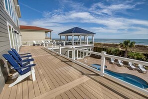 A wooden deck with lounge chairs, a pool, and a gazebo overlooking the ocean.