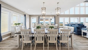 A spacious dining area with a large table and chairs, surrounded by large windows offering ocean views.