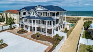 A multi-story house with a balcony, a driveway, and a beach view.