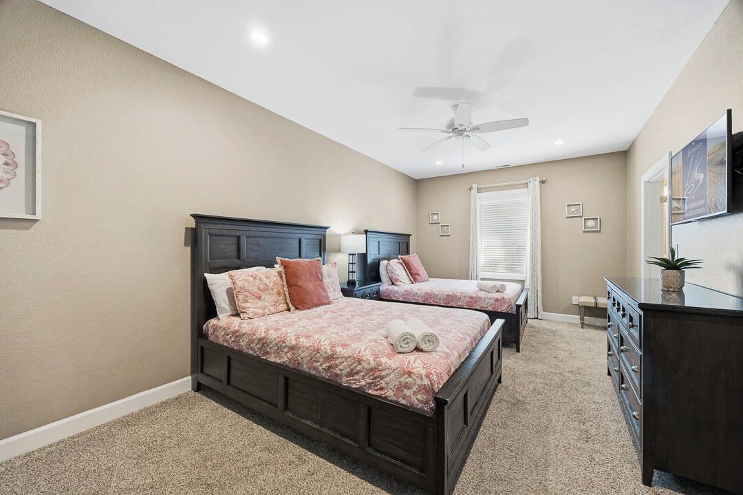Une chambre avec deux lits, un ventilateur de plafond, une commode et un téléviseur.