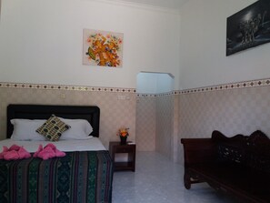 A bedroom with a bed, a nightstand, a bench, and a wall with a painting. - Citiz's House (Penida Island)