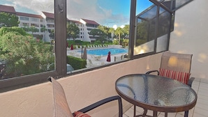 A balcony with a glass table and chairs, overlooking a swimming pool and buildings. - Spacious Condo in a Great Location! Private Beach, 2 Pools, 2 Jaccuzi, Fishing Deck & More! (Siesta Key)
