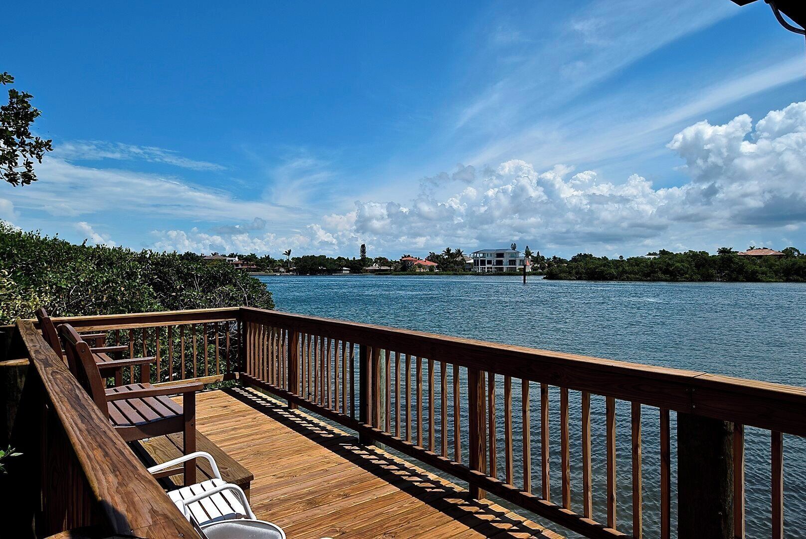 A wooden deck with a railing overlooking a body of water, with buildings and greenery in the background.