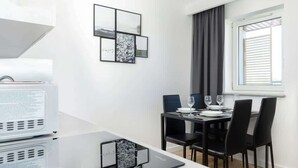 A modern dining area with a table set for two, black chairs, and a window with curtains.