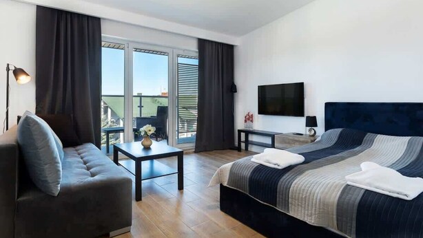A modern hotel room with a large bed, a sofa, a small table, and a TV.