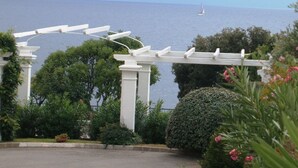 A white pergola structure with a view of the sea and a sailboat in the distance. - Studio-cabin in RDJ, with your feet in the water! (Antheor)