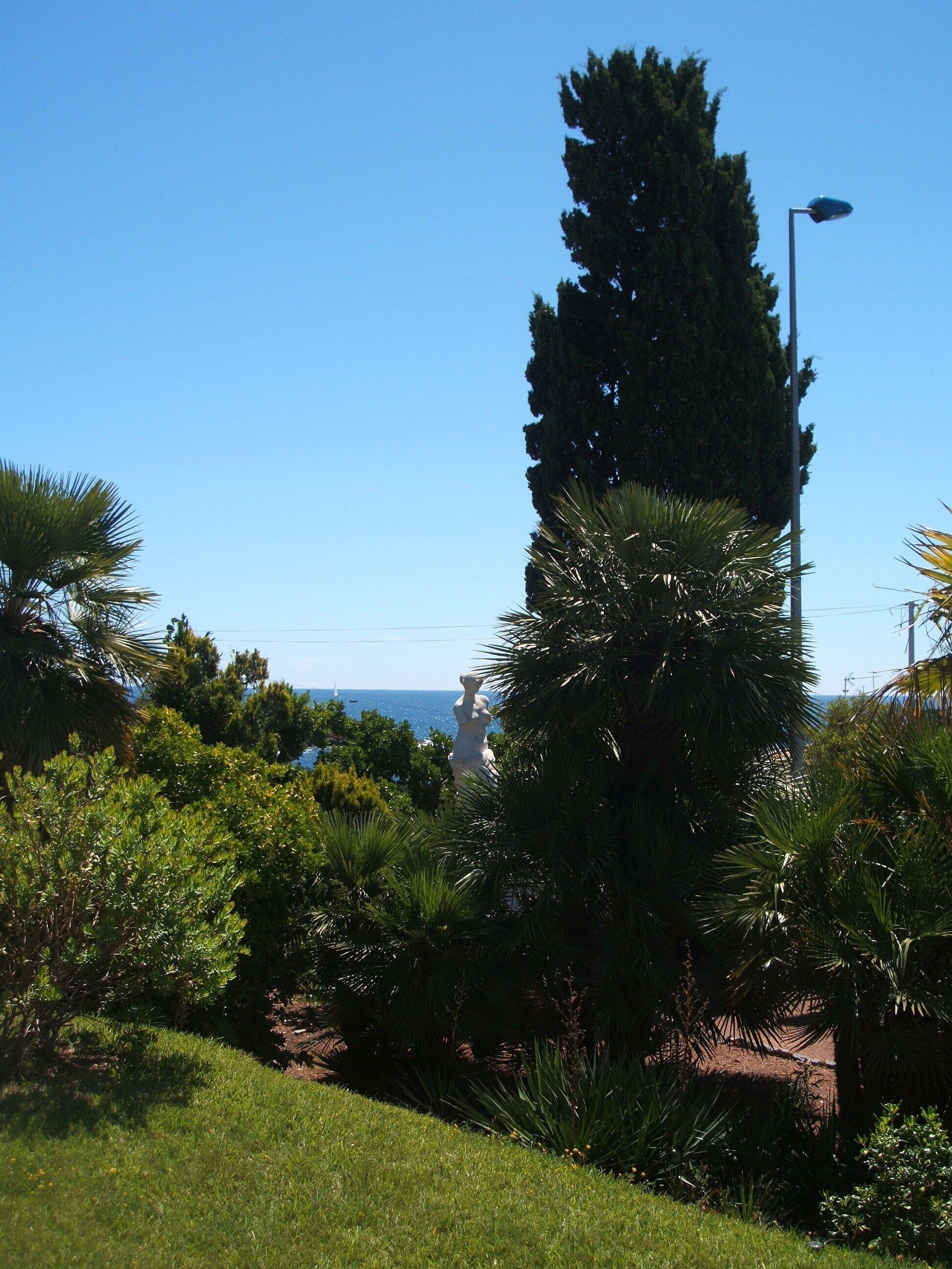 A statue in a park with a clear view of the sea in the background.
