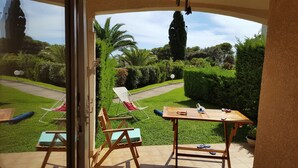 A patio area with a wooden table, two lounge chairs, and a view of a well-maintained garden with a pathway and various plants. - Studio-cabin in RDJ, with your feet in the water! (Antheor)