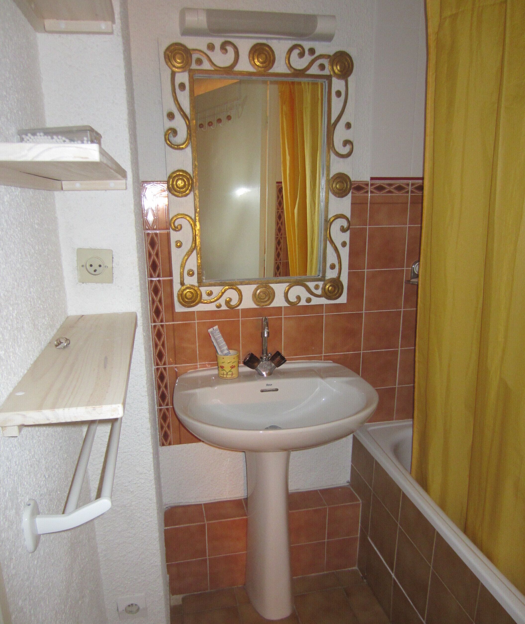 A bathroom with a pedestal sink, a mirror with ornate gold frame, and a yellow shower curtain.