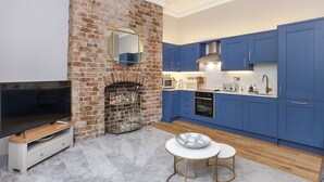 Een moderne keuken met blauwe kastjes, een met baksteen beklede open haard en een televisie in de woonkamer.