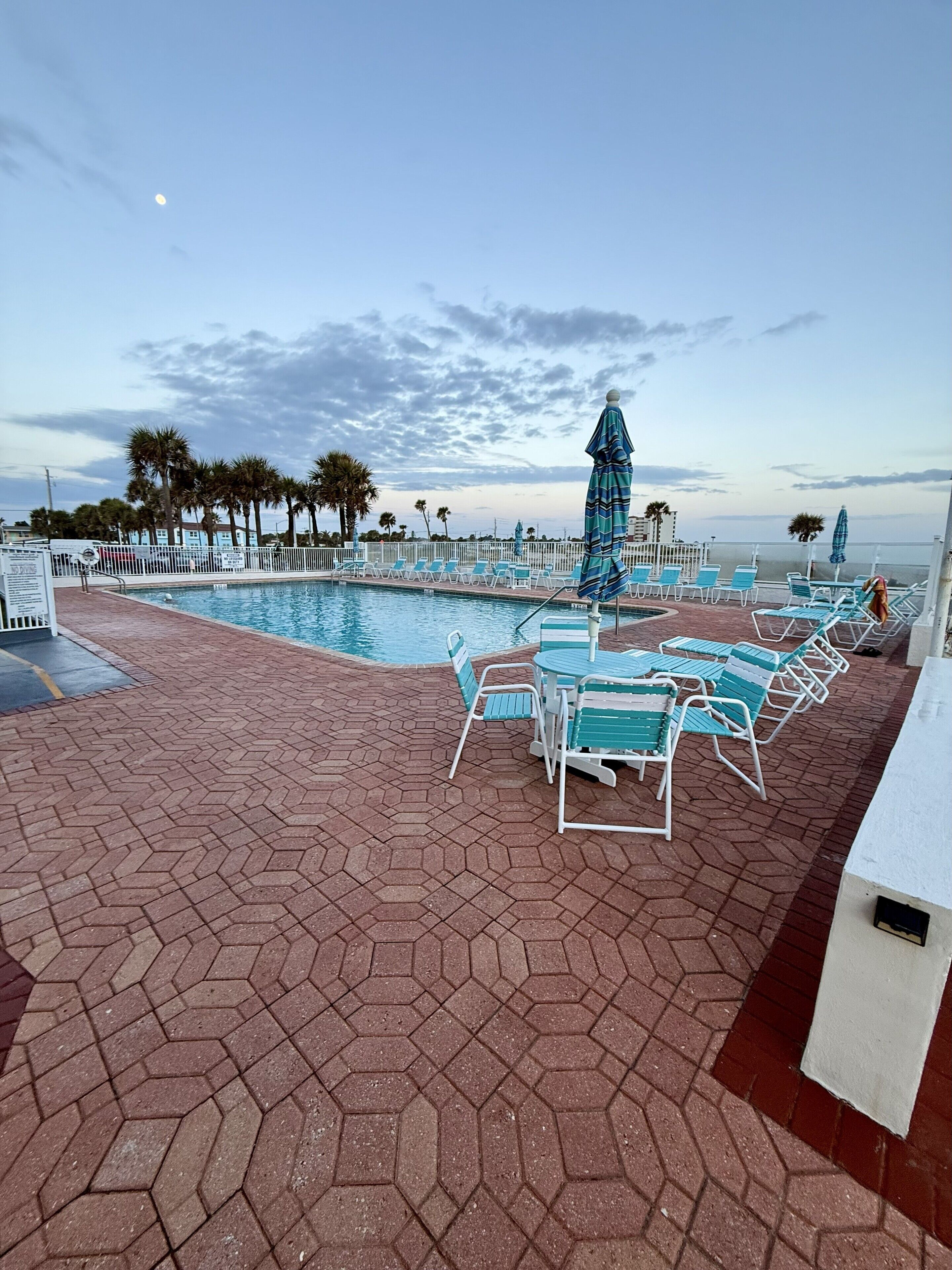 A poolside area with lounge chairs and umbrellas, a brick patio, and a view of the ocean.