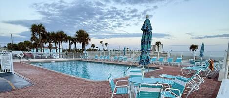 A poolside area with lounge chairs and umbrellas, a brick patio, and a view of the ocean.