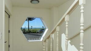 A hallway with a hexagonal window overlooking a parking area and a view of the ocean. - Marine Parade Magic - Napier Holiday Home (Napier City)