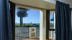A room with a large window, a view of the street, and a small balcony with a wooden floor. - Marine Parade Magic - Napier Holiday Home (Napier City)