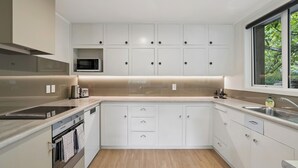 Een moderne keuken met witte kasten, een ingebouwde magnetron en een raam met uitzicht op groen.