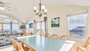 A spacious dining area with a large table and wooden chairs, large windows with curtains, and artwork on the walls. - Sea Spirit | 717 ft from the beach | Dog Friendly, Private Pool, Hot Tub | Kitty Hawk (Kitty Hawk)