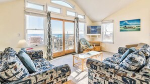 A spacious living room with a high ceiling, large windows, and a balcony with a view. - Sea Spirit | 717 ft from the beach | Dog Friendly, Private Pool, Hot Tub | Kitty Hawk (Kitty Hawk)
