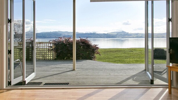 A room with a large sliding glass door leading to a deck with a view of a lake and mountains. - Lakeside Vistas Magic - Rainbow Point Home (Rainbow Point)