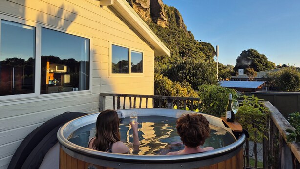 A hot tub on a balcony with a view of a mountain and a building. - Nikauscapes - Hot tub in Punakaiki Village (Punakaiki)