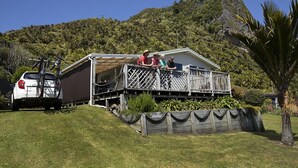 A house with a deck, a car, and a mountainous backdrop. - Nikauscapes - Hot tub in Punakaiki Village (Punakaiki)