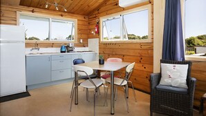 A compact kitchen with a dining area, wooden walls, and a view through the windows. - Nikauscapes - Hot tub in Punakaiki Village (Punakaiki)