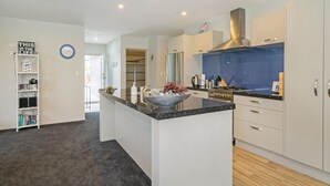 A modern kitchen with white cabinetry, a granite countertop, and stainless steel appliances. - The Blue Rendevous - Whangamata Holiday Home (Whangamata)