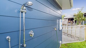 A blue exterior wall with a metal showerhead and hose. - The Blue Rendevous - Whangamata Holiday Home (Whangamata)