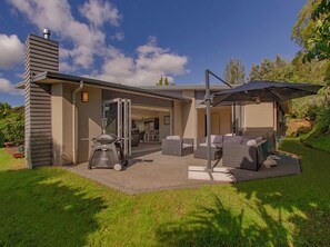 A modern house with a patio area featuring outdoor furniture and a grill. - Cooks Getaway - Cooks Beach Holiday Home (Cooks Beach)