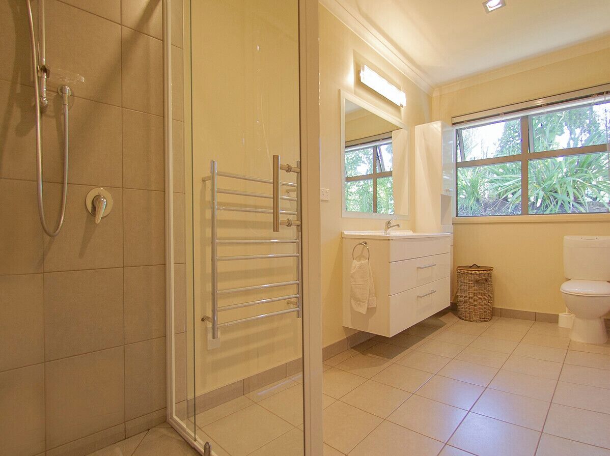 Une salle de bain avec une douche à parois de verre, un lavabo blanc, des toilettes et une fenêtre donnant sur un espace verdoyant.