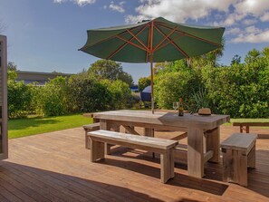 A wooden deck with a picnic table and benches, surrounded by lush greenery. - Cooks Getaway - Cooks Beach Holiday Home (Cooks Beach)